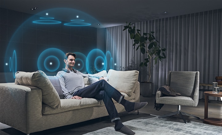 Man sitting on sofa experiencing 360 Spatial Sound using SRS-NS7 wearable speaker and WLA-NS7 wireless transmitter